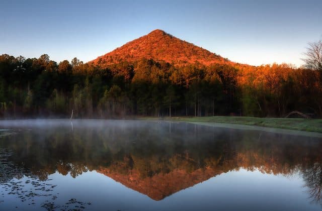 A mountain reflects in a tranquil lake surrounded by trees at dawn.