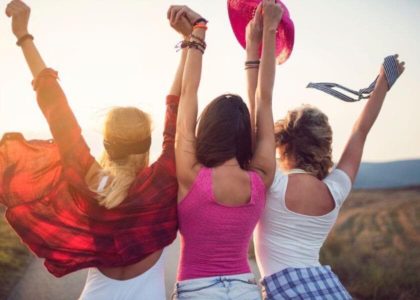 Three friends raise their arms joyfully while standing in a sunlit field. Three friends raise their arms joyfully while standing in a sunlit field.