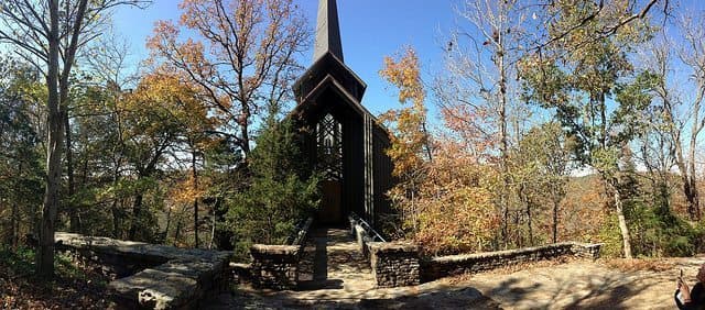 A modern church surrounded by autumn foliage against a clear blue sky.