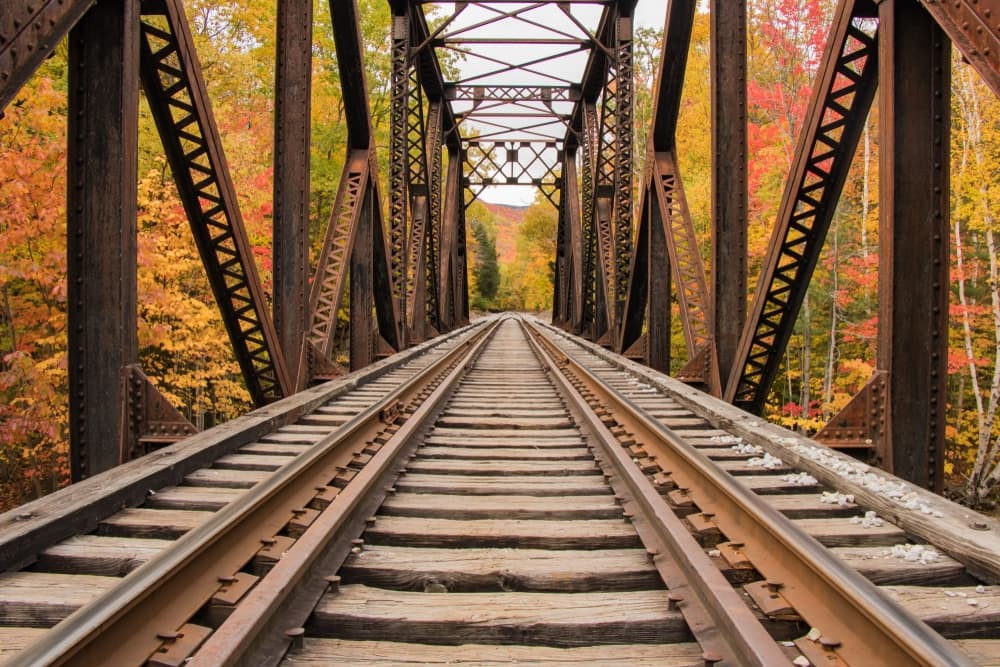 View down a railway track across a bridge surrounded by autumn foliage.