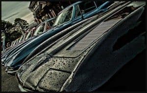 A row of vintage cars with raindrops on their hoods, capturing a reflective surface and moody lighting.