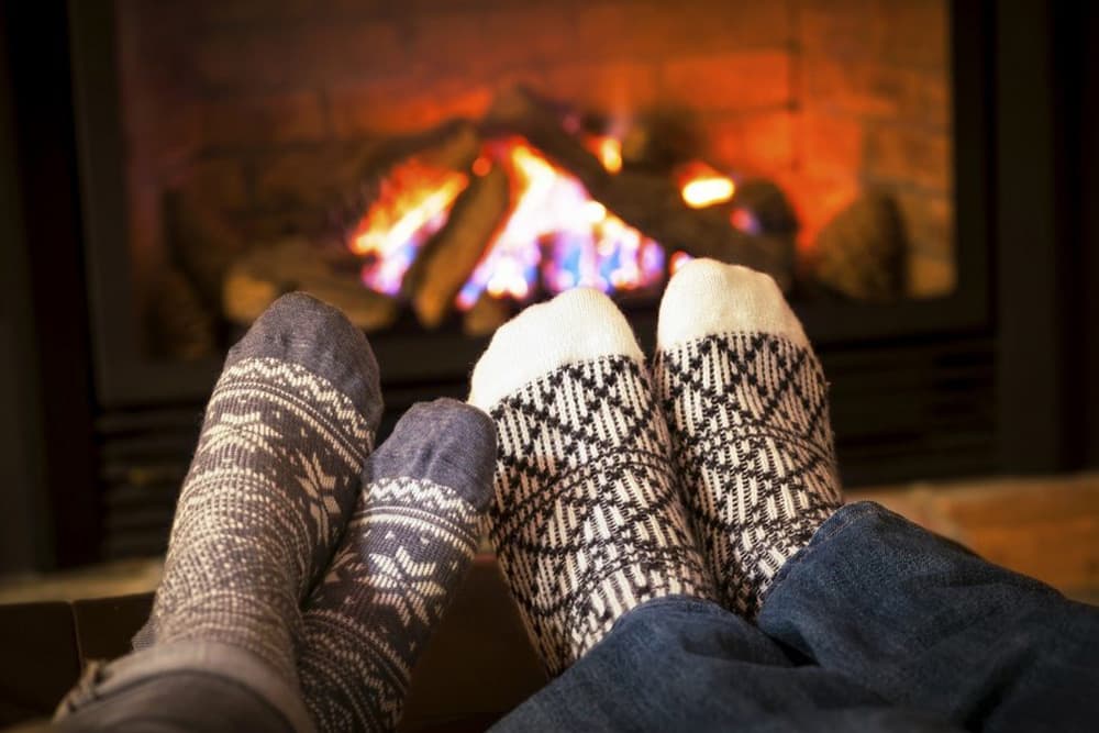 A cozy and inviting image of two people wearing warm socks, relaxing by a fireplace. The flames dance brightly, creating a warm and inviting atmosphere.
