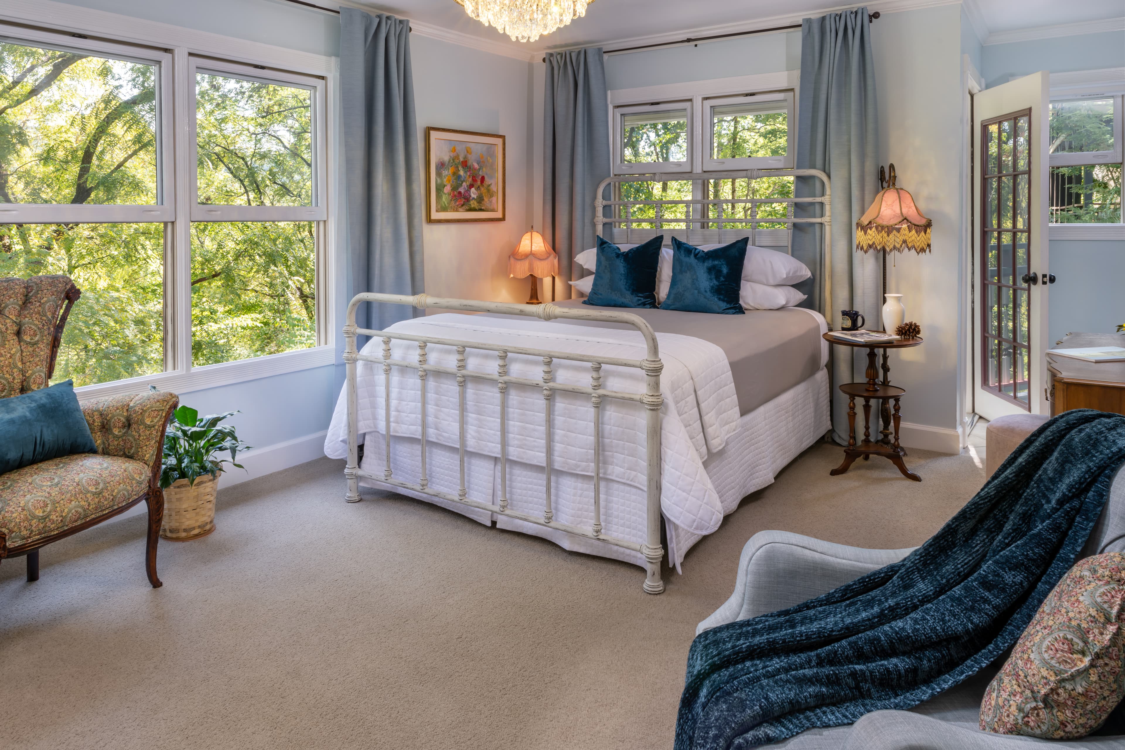 Cozy bedroom featuring a metal bed frame, plush pillows, and large windows with a view of greenery.