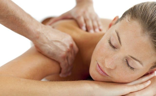 A woman receiving a back massage with eyes closed in a relaxed position.