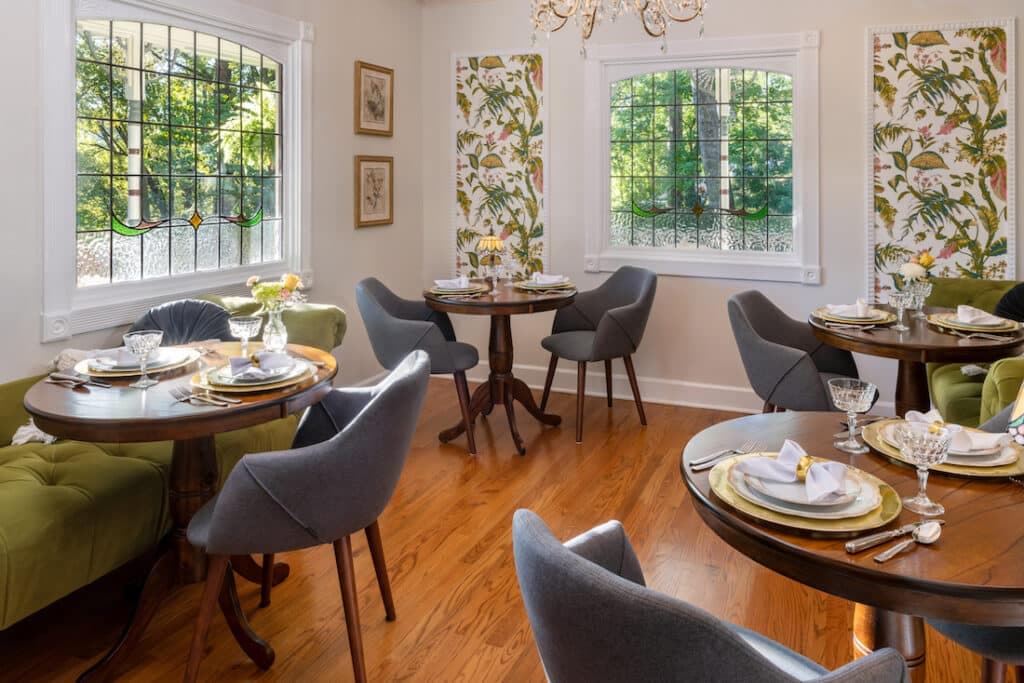 A bright dining room featuring round wooden tables, gray chairs, and floral wallpaper.