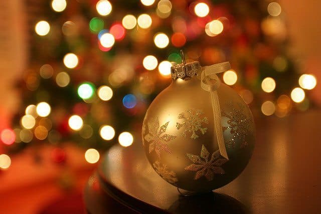 A gold Christmas ornament sits on a table, with a softly blurred tree and colorful lights in the background. A gold Christmas ornament sits on a table, with a softly blurred tree and colorful lights in the background.