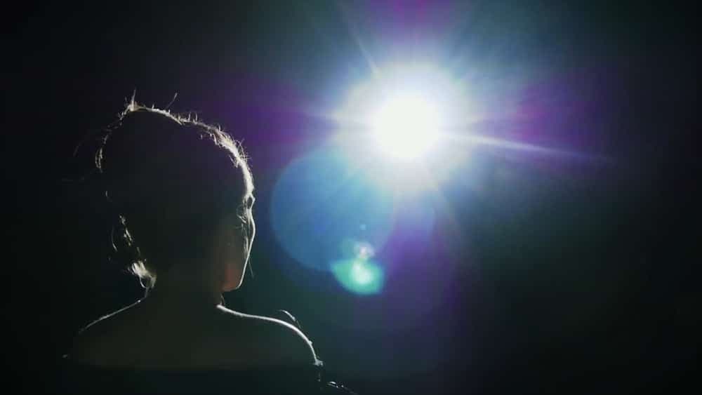 A silhouette of a woman is illuminated by a bright spotlight against a dark background.