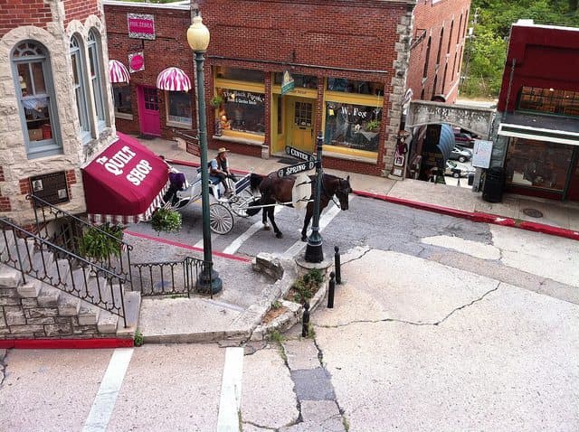 A horse-drawn carriage navigates a quaint, sloped street lined with historic buildings and shops.