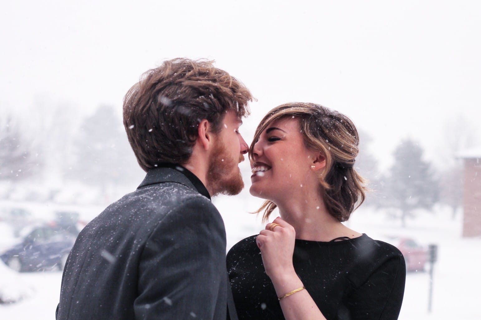 A couple shares a joyful moment while snow falls around them.
