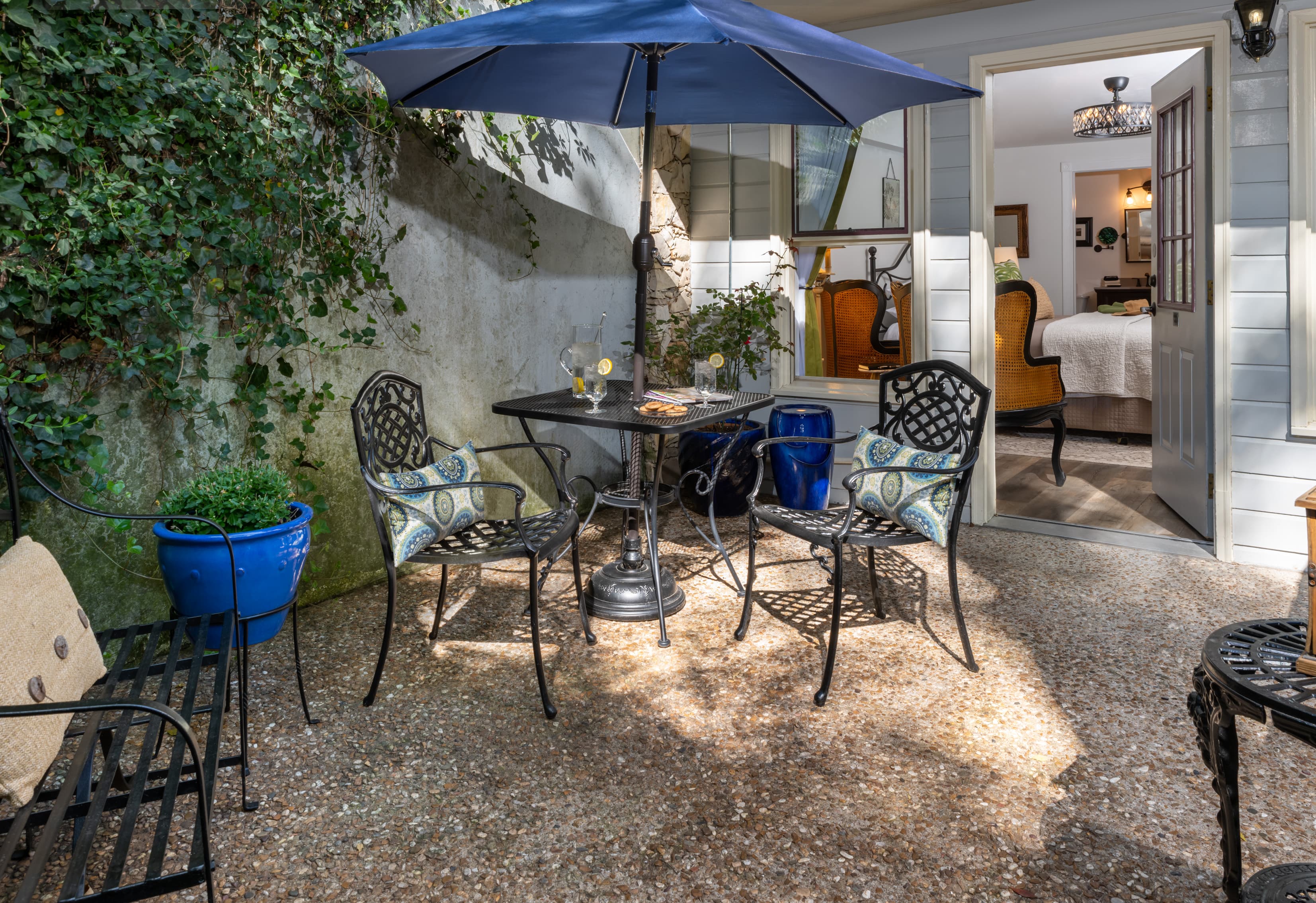 A cozy outdoor seating area features a table with two chairs under an umbrella, surrounded by greenery.