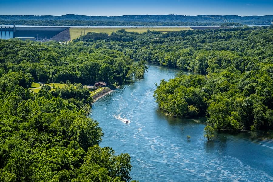 A boat navigates a winding river surrounded by lush green forests and hills.