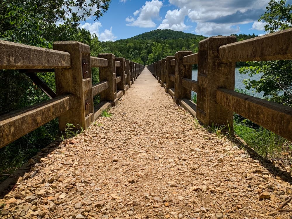 A wide gravel path leads between stone barriers toward a distant green hill under a blue sky with fluffy clouds. A wide gravel path leads between stone barriers toward a distant green hill under a blue sky with fluffy clouds.