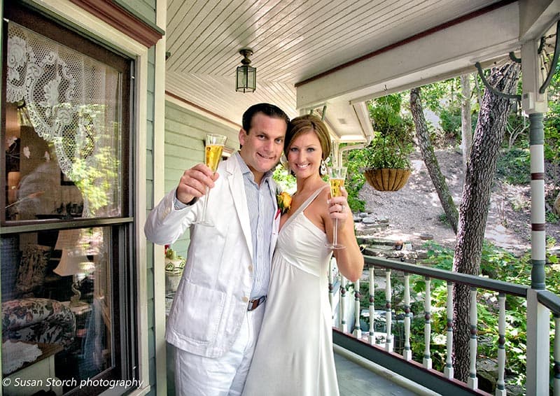 A newly married couple holds champagne glasses while celebrating on a porch.